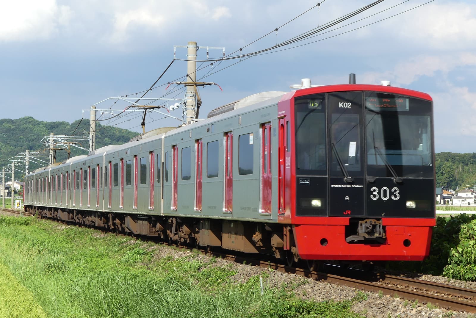 A red-fronted JR Chikuhi Line train running through the Itoshima countryside