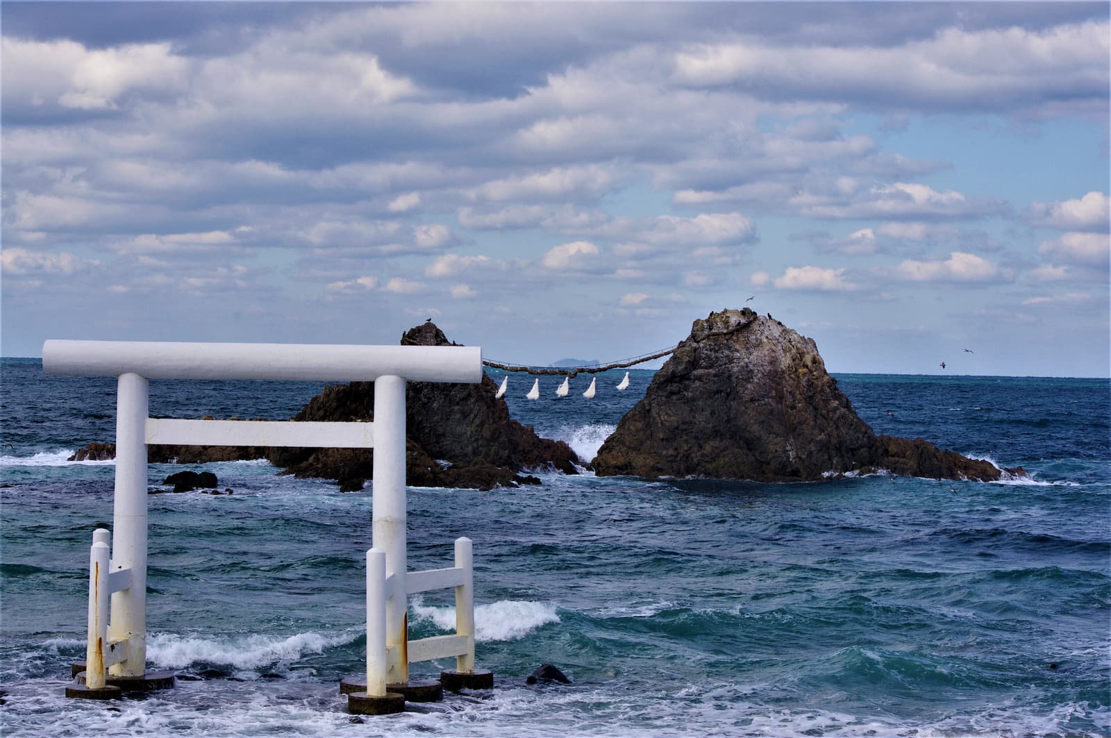 The white torii and the rope-linked married rocks at Sakurai Futamigaura in rough seas
